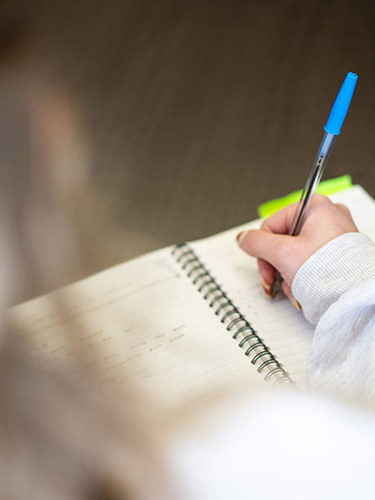 A close up of a hand writing on a pad with a biro